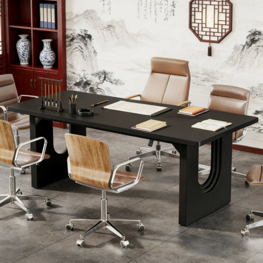 Black modern conference table with curved base legs in minimalist office setting with Asian-inspired wall art.